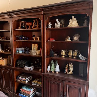 Large dark wood multi-unit wall system featuring open bookshelves above lower cabinet doors, filled with various collectibles, glassware,...