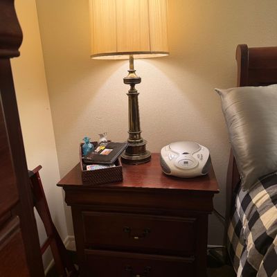 Traditional dark wood two-drawer nightstand topped with a brass table lamp and a portable CD player boombox.