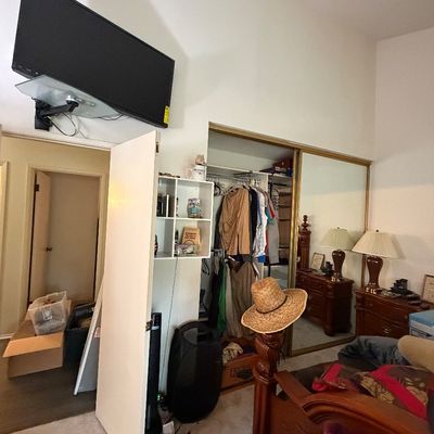 Bedroom setup featuring a wall-mounted flat-screen television above a white door, alongside traditional dark wood furniture and a sliding...