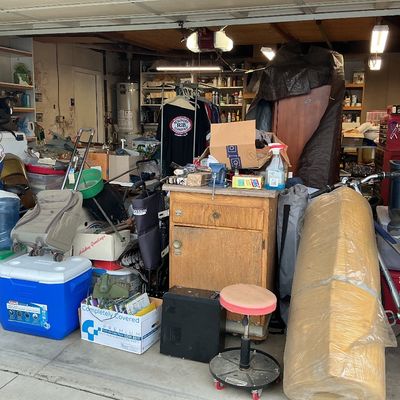 Sale Photo Thumbnail #126: Crowded garage full of household items, including a blue Coleman cooler, rolled foam, a vintage bicycle, a rolling workshop stool, and a wooden cabinet.