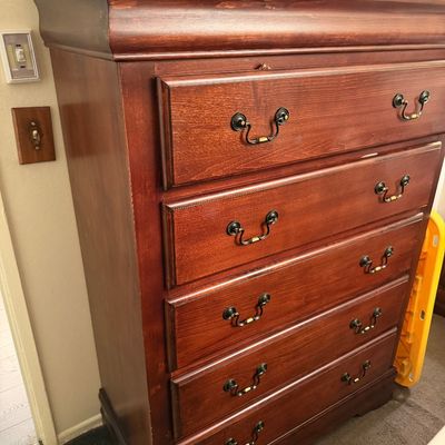 Traditional cherry-finished tall boy chest of drawers featuring decorative metal bail handles and minor finish wear along the top edge.