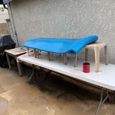 Blue foam pool lounge float sitting atop folding tables and plastic patio stools outdoors.