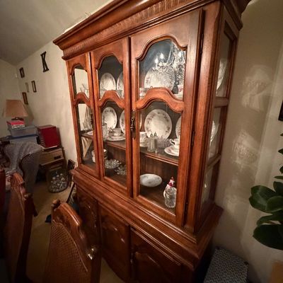 Traditional wooden china cabinet with glass-paneled doors, arched details, and lower storage drawers, filled with ceramic dishware.