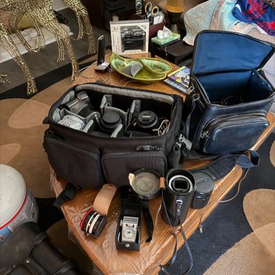 Collection of photography equipment including two padded camera bags containing Canon DSLR bodies and lenses, alongside vintage light...