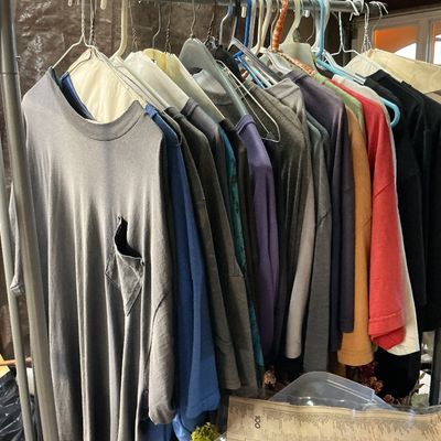 Sale Photo Thumbnail #129: Clothing rack filled with an assortment of vintage men's T-shirts and long-sleeve shirts in various colors.