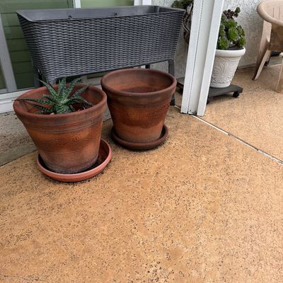 Collection of outdoor planters, featuring two large terracotta pots with saucers, a succulent, and a raised grey wicker-pattern planter box.