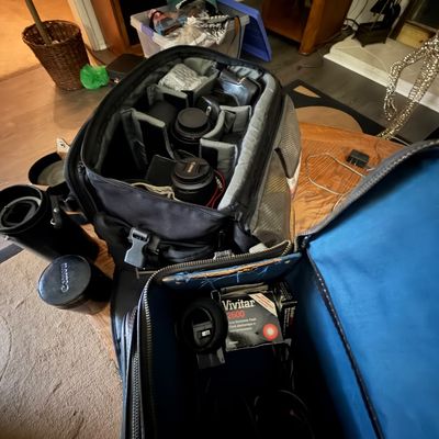 Open black camera gear backpacks filled with various lenses, accessories, and a Vivitar 2600 electronic flash unit in its original box.