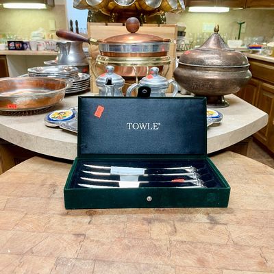 Sale Photo Thumbnail #2: Boxed set of Towle stainless steel steak knives displayed on a wooden butcher block alongside copper and brass servingware