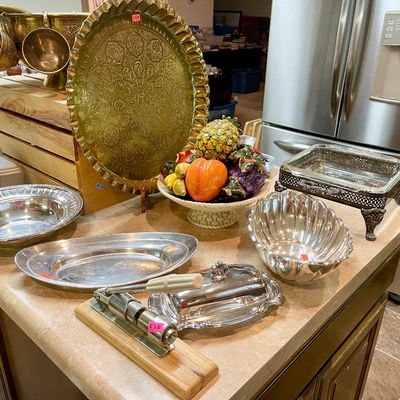 Sale Photo Thumbnail #3: Collection of metal serving ware and decor, featuring an ornate brass tray, silver-tone platters, a punch bowl set, and a ceramic fruit basket displayed