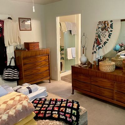 Sale Photo Thumbnail #10: Bedroom featuring mid-century modern walnut dressers, a large wall mirror, vintage linens and blankets, hanging clothing, and various decorative accents