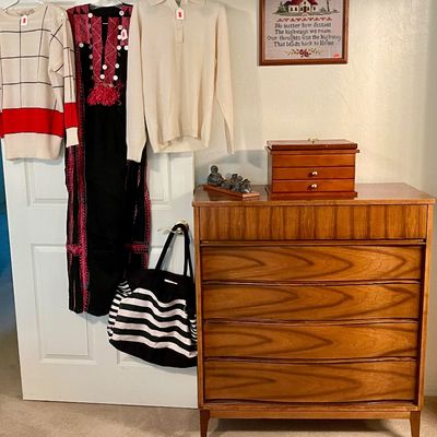 Sale Photo Thumbnail #12: Mid-century modern teak tallboy chest of drawers paired with a wooden jewelry box, hanging vintage sweaters, an embroidered gown, and a striped tote bag
