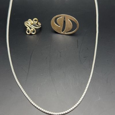 Set of modern sterling silver jewelry including a box chain necklace, a scrollwork ring, and a cutout oval pendant.