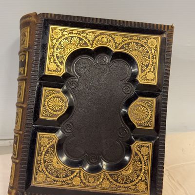 Antique 19th-century leather-bound book featuring ornate gilt-tooled patterns and a raised, deeply recessed central panel with scrollwork...