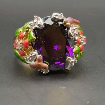 Statement cocktail ring featuring a large oval faceted purple stone set in an ornate enamel floral shank.