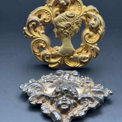 Pair of ornate Art Nouveau metal dresser or furniture ornaments, including a gold-tone lady's cameo profile and a silvered cherub...