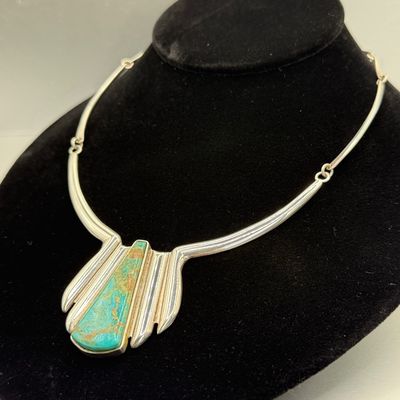 Southwestern-style sterling silver collar necklace featuring a central fan pendant inlaid with a natural turquoise cabochon displayed on...