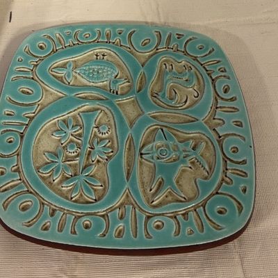 Mid-century modern turquoise ceramic trivet or wall plaque with stylized relief carvings of fish and flora.