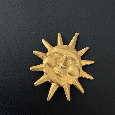 Sale Photo Thumbnail #154: A vintage gold-tone celestial brooch featuring a stylized smiling sun face with radiating rays. The pin features a standard rollover safety clasp on the back. Shows minor surface wear and light patina consistent with age.