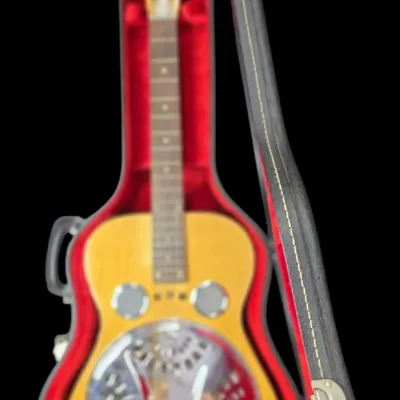 Sale Photo Thumbnail #26: Vintage Dobro resonator acoustic guitar with a natural finish body, ornate metal resonator plate, and fitted red plush-lined hard case.