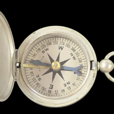 Sale Photo Thumbnail #110: Vintage pocket watch-style directional compass in a silver-tone metal hinged casing.