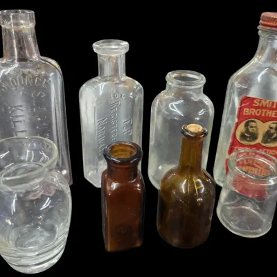 Sale Photo Thumbnail #86: Collection of vintage glass apothecary and medicine bottles, including embossed Sloan's Liniment and Smith Brothers Cough Syrup with an original label.