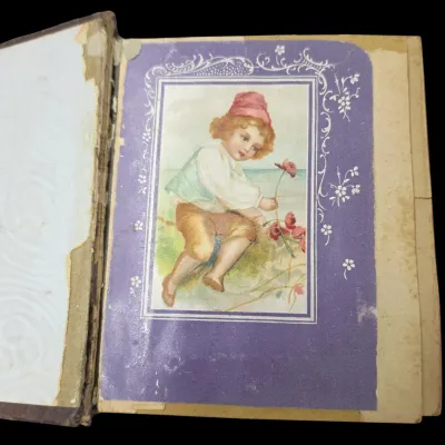 Sale Photo Thumbnail #94: Antique photo album page featuring a Victorian chromolithograph trade card or scrap depicting a child with flowers, set within a decorative purple border.