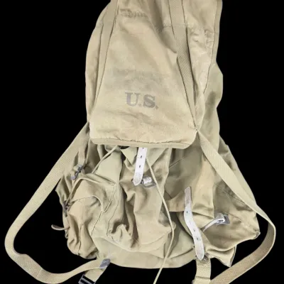 Sale Photo Thumbnail #56: Vintage U.S. military canvas field backpack featuring stamped "U.S." lettering on the top flap, webbed shoulder straps, and metal buckle closures.