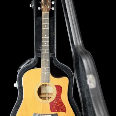 Sale Photo Thumbnail #27: Taylor acoustic-electric guitar with natural finish top and tortoiseshell pickguard, resting inside a plush-lined hard shell case.
