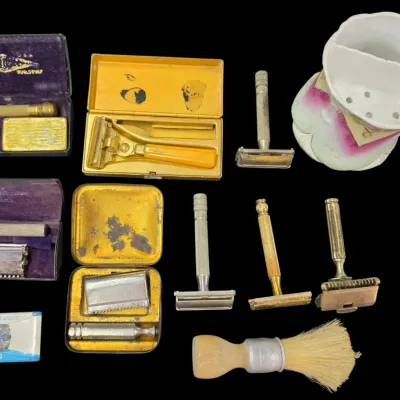 Sale Photo Thumbnail #80: Collection of vintage safety razors, brass and metal cases, a shaving brush, Gillette Super Blue Blades, and a floral ceramic scuttle mug.