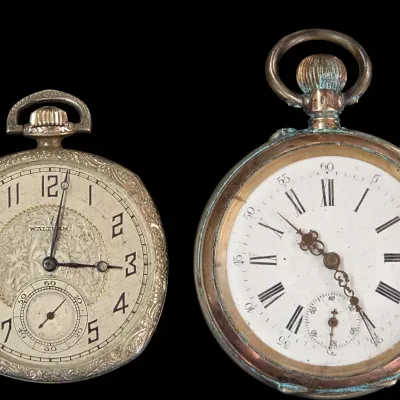 Sale Photo Thumbnail #126: Pair of antique pocket watches, including an engraved Waltham watch with an Art Deco face and a heavily patinated brass watch with Roman numerals.