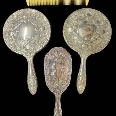 Sale Photo Thumbnail #163: Vintage silver-plated vanity set featuring two handheld mirrors, a hairbrush, and a comb with intricate floral repoussé scrollwork, showing minor age-appropriate tarnishing.