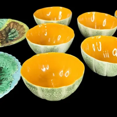 Sale Photo Thumbnail #51: Vintage majolica ceramic tableware set featuring melon-shaped bowls with bright orange interiors alongside textured green leaf-motif plates.