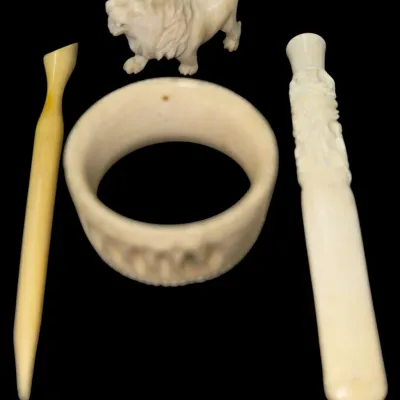 Sale Photo Thumbnail #137: Collection of carved cream-colored items, including a lion figurine, a carved bangle bracelet, a slender tool, and an ornate cigarette holder.