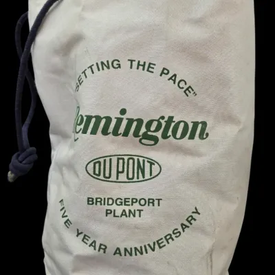 Sale Photo Thumbnail #74: Vintage canvas duffle bag featuring green graphics for 'Remington DuPont Bridgeport Plant Five Year Anniversary', equipped with a rope drawstring closure.