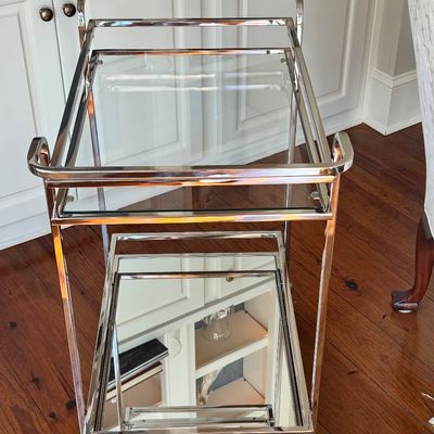 Sale Photo Thumbnail #269: A sleek, minimalist bar cart characterized by a polished chrome-plated metal frame and dual -tier shelving. The upper tier is a clear glass surface, while the lower tier is fitted with a mirrored glass shelf, providing a sophisticated reflected quality. T