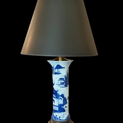 Sale Photo Thumbnail #136: A sophisticated pair of table lamps featuring cylindrical porcelain bodies decorated in classic blue and white landscape pattern, depicting pagodas and mountainous scenery. The porcelain bases are mounted on carved wooden stands and topped with modern bra