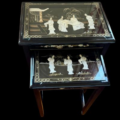 Sale Photo Thumbnail #170: Vintage Chinese nesting tables featuring a deep black lacquer finish with intricate applied porcelain figurines. Each table top is protected with a glass insert depicting East Asian scenes. The tables are constructed with clean, minimalist lines typical o