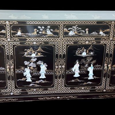 Sale Photo Thumbnail #177: A large black lacquer and mother-of-pearl inlaid figural sideboard depicting the popular “Royal Ladies” narrative scene. Constructed with four central cabinet doors and four upper drawers. The craftsmanship reflects the traditional East Asian furnitur