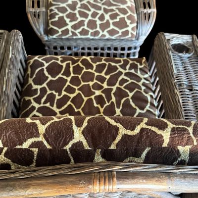 Sale Photo Thumbnail #293: Constructed from woven wicker and rattan, featuring a distinctive, wide-arm design with an integrated circular cup holder on the right armrest. The chair is upholstered in bold, animal-print fabric featuring a giraffe-inspired pattern. Its structural comp