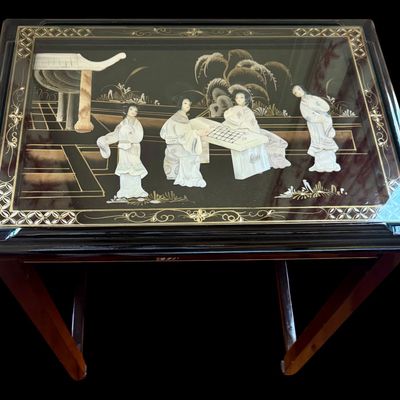 Sale Photo Thumbnail #173: Vintage Chinese nesting tables featuring a deep black lacquer finish with intricate applied porcelain figurines. Each table top is protected with a glass insert depicting East Asian scenes. The tables are constructed with clean, minimalist lines typical o