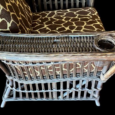 Sale Photo Thumbnail #290: Constructed from woven wicker and rattan, featuring a distinctive, wide-arm design with an integrated circular cup holder on the right armrest. The chair is upholstered in bold, animal-print fabric featuring a giraffe-inspired pattern. Its structural comp