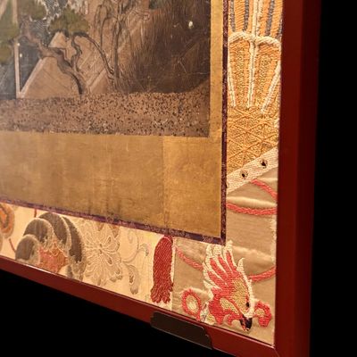 Sale Photo Thumbnail #6: Impressive Japanese eight-panel folding screen featuring hand painted narrative scenes of figures in traditional dress, architecture, and landscapes in muted earth tones with colorful accents. The paintings are framed by gold tone borders, decorative silk