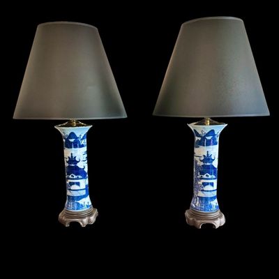 Sale Photo Thumbnail #135: A sophisticated pair of table lamps featuring cylindrical porcelain bodies decorated in classic blue and white landscape pattern, depicting pagodas and mountainous scenery. The porcelain bases are mounted on carved wooden stands and topped with modern bra