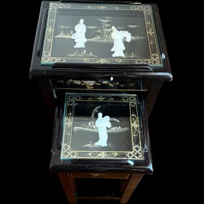 Sale Photo Thumbnail #172: Vintage Chinese nesting tables featuring a deep black lacquer finish with intricate applied porcelain figurines. Each table top is protected with a glass insert depicting East Asian scenes. The tables are constructed with clean, minimalist lines typical o