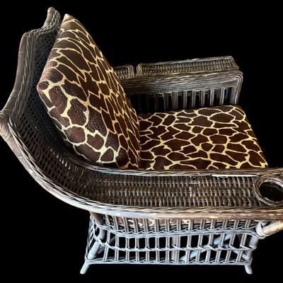 Sale Photo Thumbnail #289: Constructed from woven wicker and rattan, featuring a distinctive, wide-arm design with an integrated circular cup holder on the right armrest. The chair is upholstered in bold, animal-print fabric featuring a giraffe-inspired pattern. Its structural comp