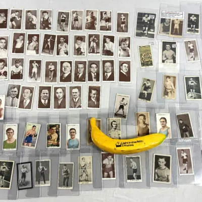 Sale Photo Thumbnail #14: Large collection of vintage boxing trading cards, featuring monochrome and full-color portraits, many displayed in protective sleeves alongside a yellow scale banana.