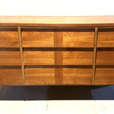 Sale Photo Thumbnail #16: Mid-century modern walnut nine-drawer dresser featuring integrated wood pulls and tapered peg legs, showing light surface wear.