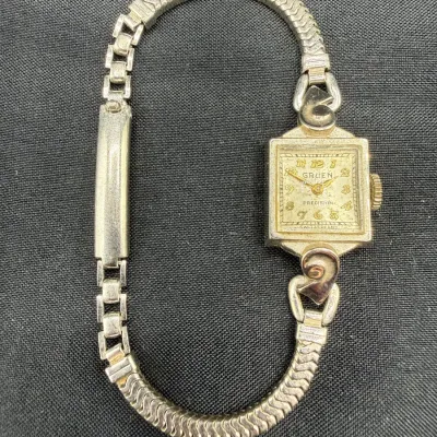 Sale Photo Thumbnail #24: Vintage Gruen Precision ladies' wristwatch with a square case, gold-tone Arabic numerals, decorative scroll lugs, and an expandable silver-tone band.