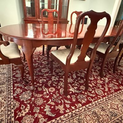 Sale Photo Thumbnail #12: Traditional Queen Anne style mahogany dining set including an oval extension table and matching splat-back chairs with cream upholstered seats, displayed over an oriental-patterned area rug.