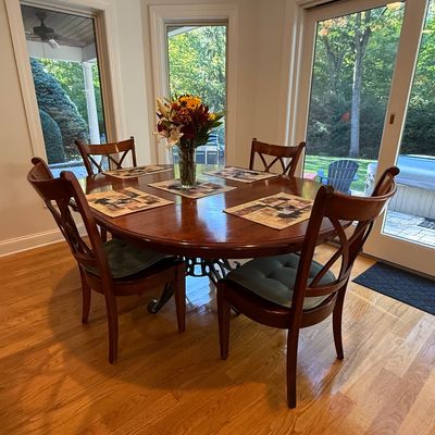 Sale Photo Thumbnail #7: Round polished wood dining table set with four matching cross-back chairs and green seat cushions, placed in a bright breakfast nook.
